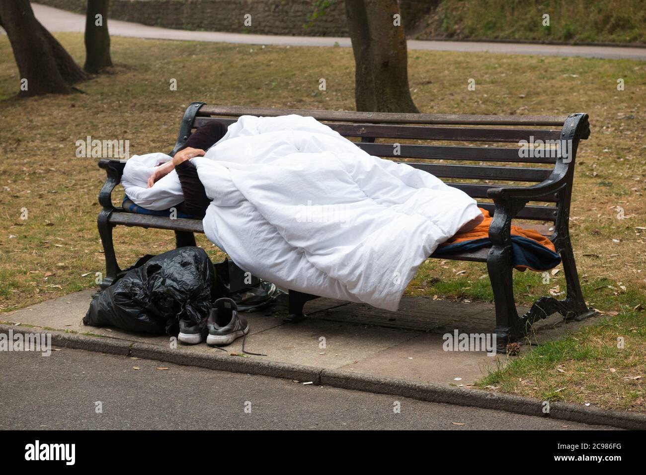 Ein anonymer und ein nicht identifizierbarer obdachloser Mann schlafen auf einer Parkbank in einem öffentlichen Raum. Bournemouth, England, Großbritannien. (120) Stockfoto