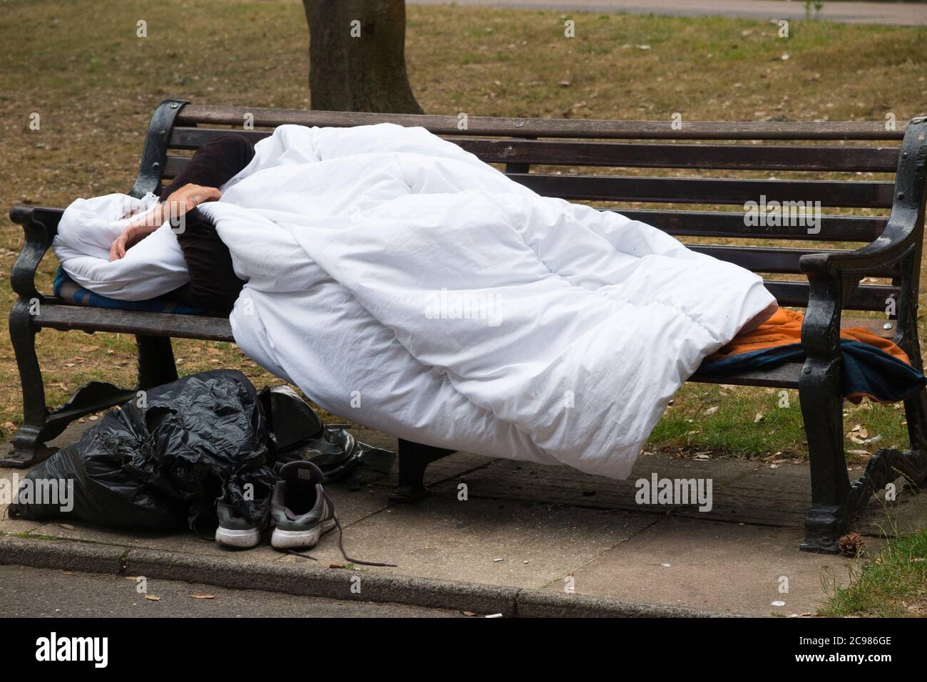 Ein anonymer und ein nicht identifizierbarer obdachloser Mann schlafen auf einer Parkbank in einem öffentlichen Raum. Bournemouth, England, Großbritannien. (120) Stockfoto