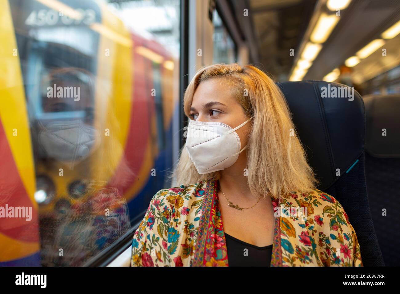 Ein blondes Mädchen mit Gesichtsmaske sitzt in einem Zugwagen in Waterloo Station, London, 26. Juli 2020 Stockfoto