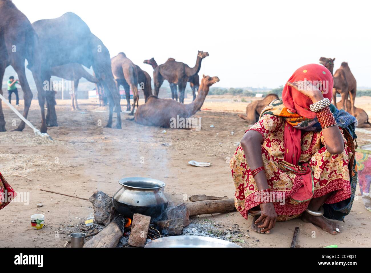 Ndian junge Dame mit Familie warm, indem sie in der Nähe des bon Feuer am frühen Morgen auf pushkar Kamel Messe Boden sitzen. Stockfoto