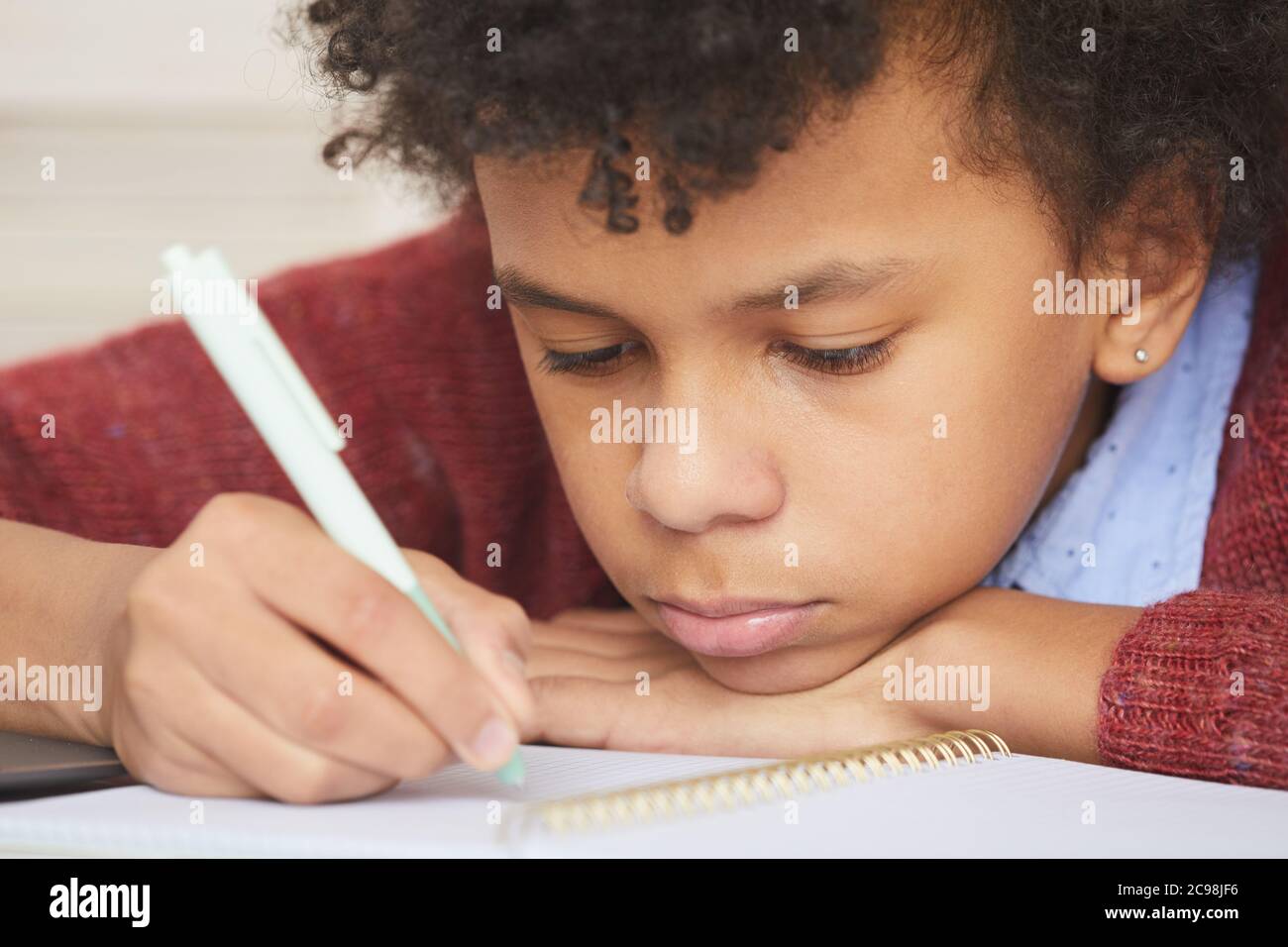 Nahaufnahme eines ernsthaften afrikanischen Jungen, der sich auf das Studium konzentriert und am Schreibtisch sitzt und Papierkram macht Stockfoto