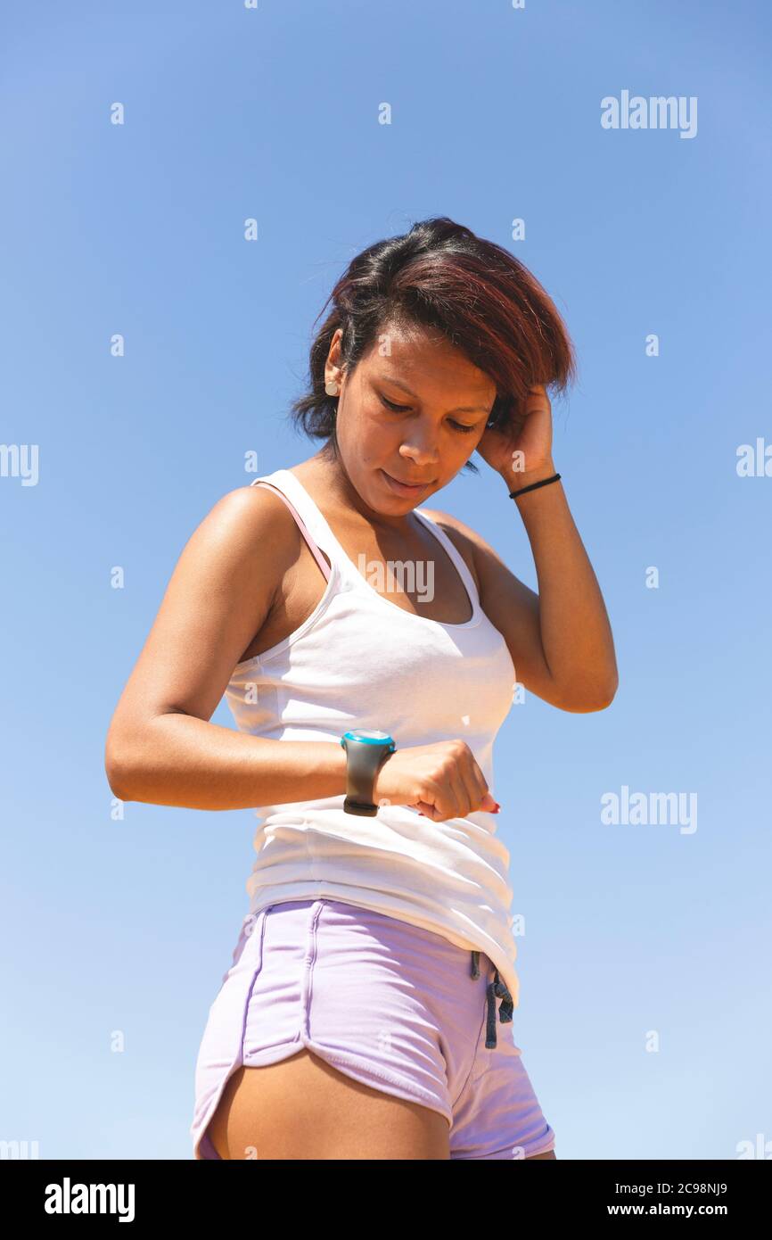 Porträt einer Sportlerin, die auf eine Stoppuhr schaut. Sie ist draußen und trägt ein Tanktop und Shorts. Leerzeichen für Text. Stockfoto