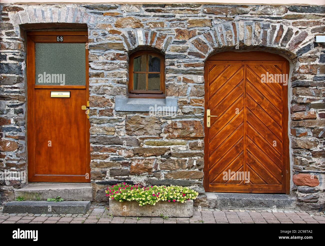 Zwei Holztüren, verschiedene Stile, altes Steingebäude, kleines Fenster dazwischen, Blumen in Steinpflanzer, Europa; Zell, Deutschland Stockfoto