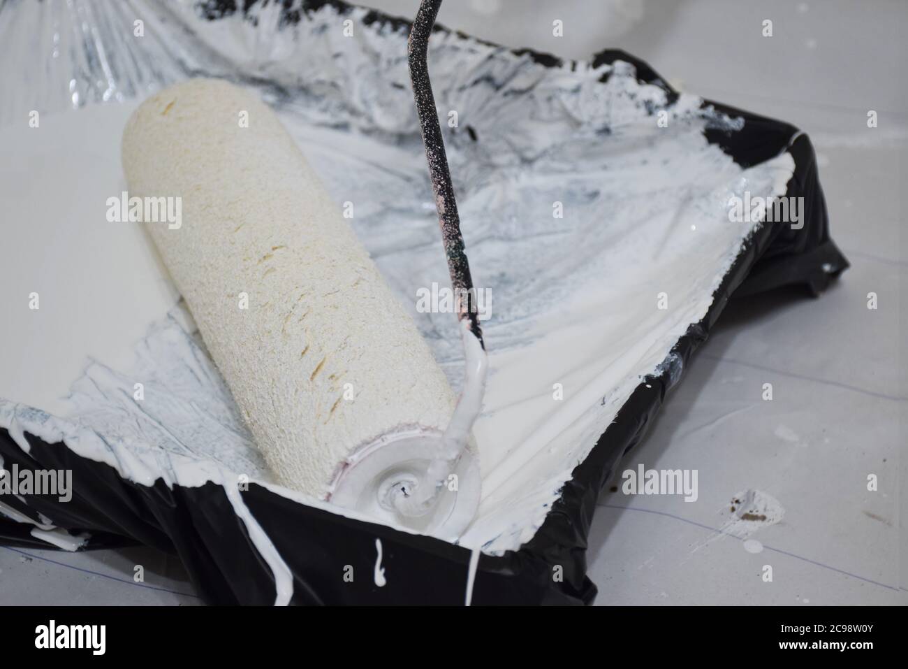 Pinsel für die Malrolle: Weiße Farbe auf dem Farbtablett durcheinander bringen. Stockfoto