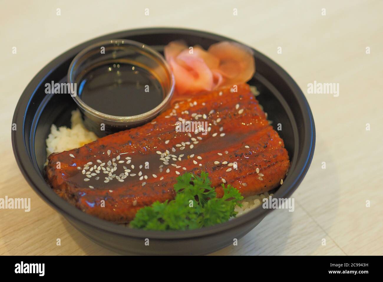 Unadon oder unagi Donburi mit eingelegtem Ingwer in schwarzer Kunststoffschale zum Mitnehmen. Stockfoto