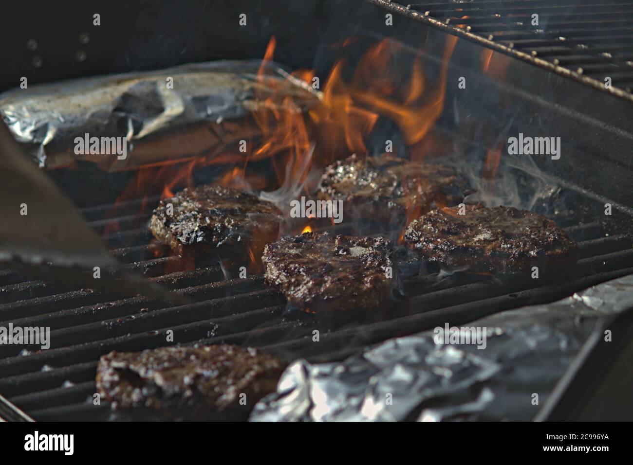 Eine Person, die Burger auf dem Grill mit Flammen dreht Stockfoto