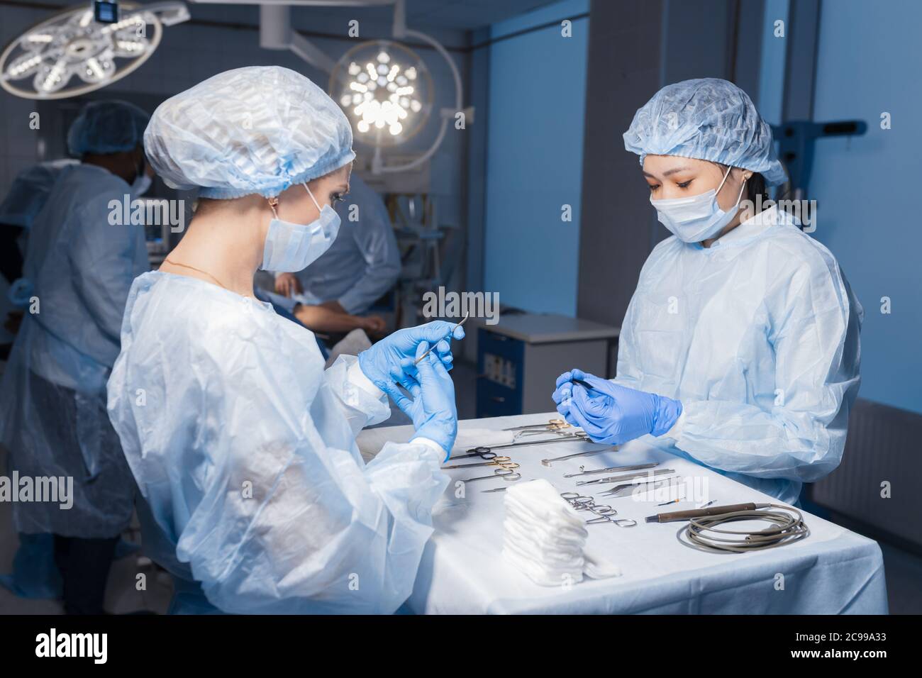 Zwei jungen asiatischen und Kaukasische weiblichen Assistenten Vorbereitung chirurgische Instrumente und Werkzeuge auf eine Tabelle für eine Operation angeordnet, mit allen notwendigen eq Stockfoto