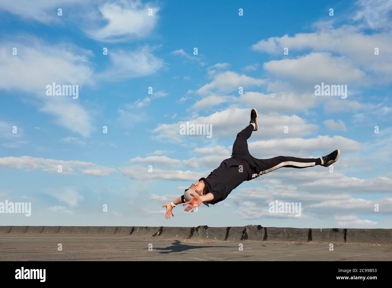 Asiatische Hip-Hop-Mann Tänzerin in schwarzen Sporthosen, Sweatshirt Springen in der Luft, machen einen Downrock Stunts im Freien auf dem Dach über blauen Himmel backgrou Stockfoto