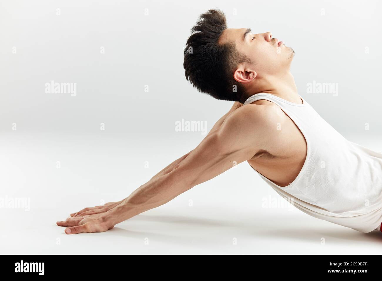 Asiatische Straßentänzerin in roten Sporthosen, die sich vor dem Training im weißen Studio aufwärmen. Stockfoto