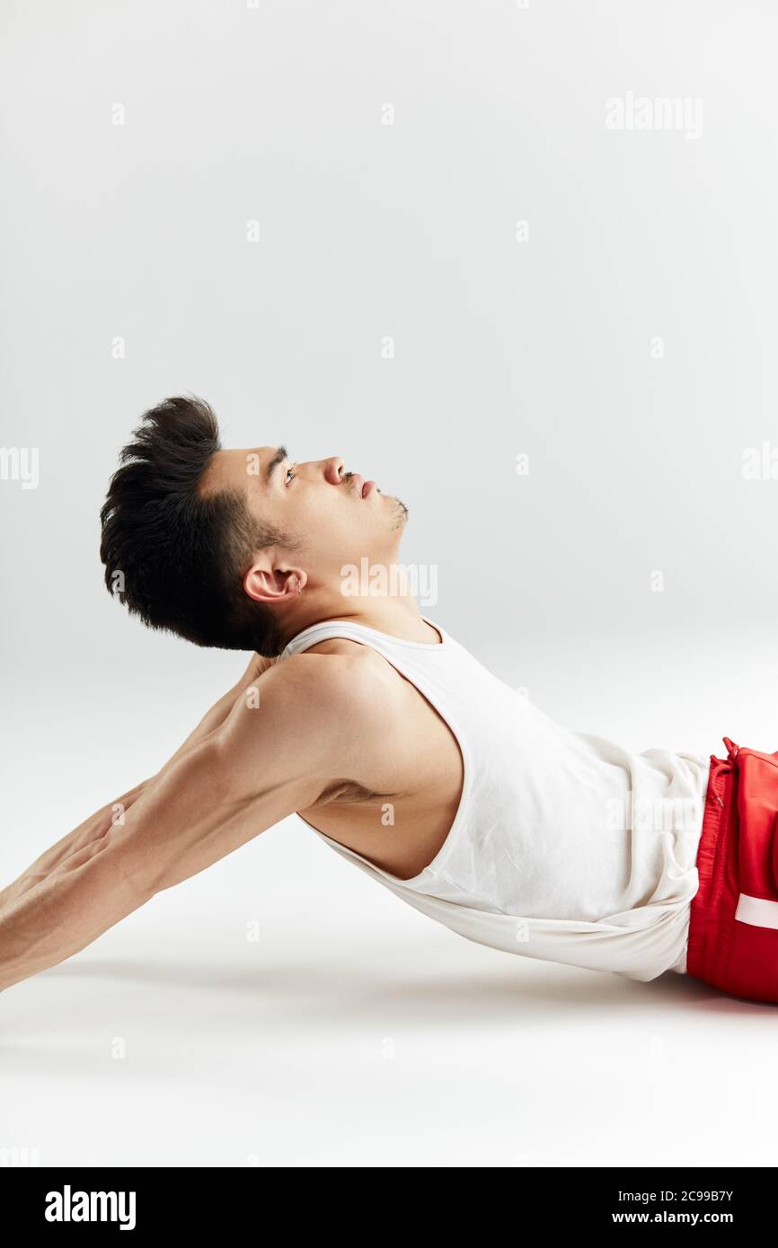 Asiatische Straßentänzerin in roten Sporthosen, die sich vor dem Training im weißen Studio aufwärmen. Stockfoto