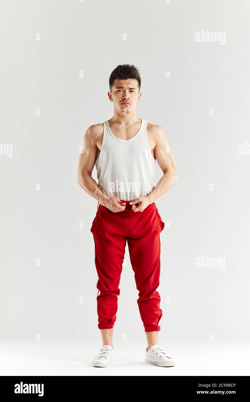 Asiatische Straßentänzerin in roten Sporthosen posiert vor dem Training im weißen Studio vor der Kamera. Stockfoto
