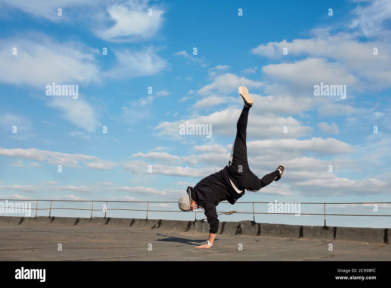 Street Dancer Hipster Kerl macht zurück Flip mit Arm Unterstützung. Asiatische Breakdancer Ausübung auf Dach. Low-Angle-Mid-Air-Ansicht vor blauem Himmel Hintergrund Stockfoto