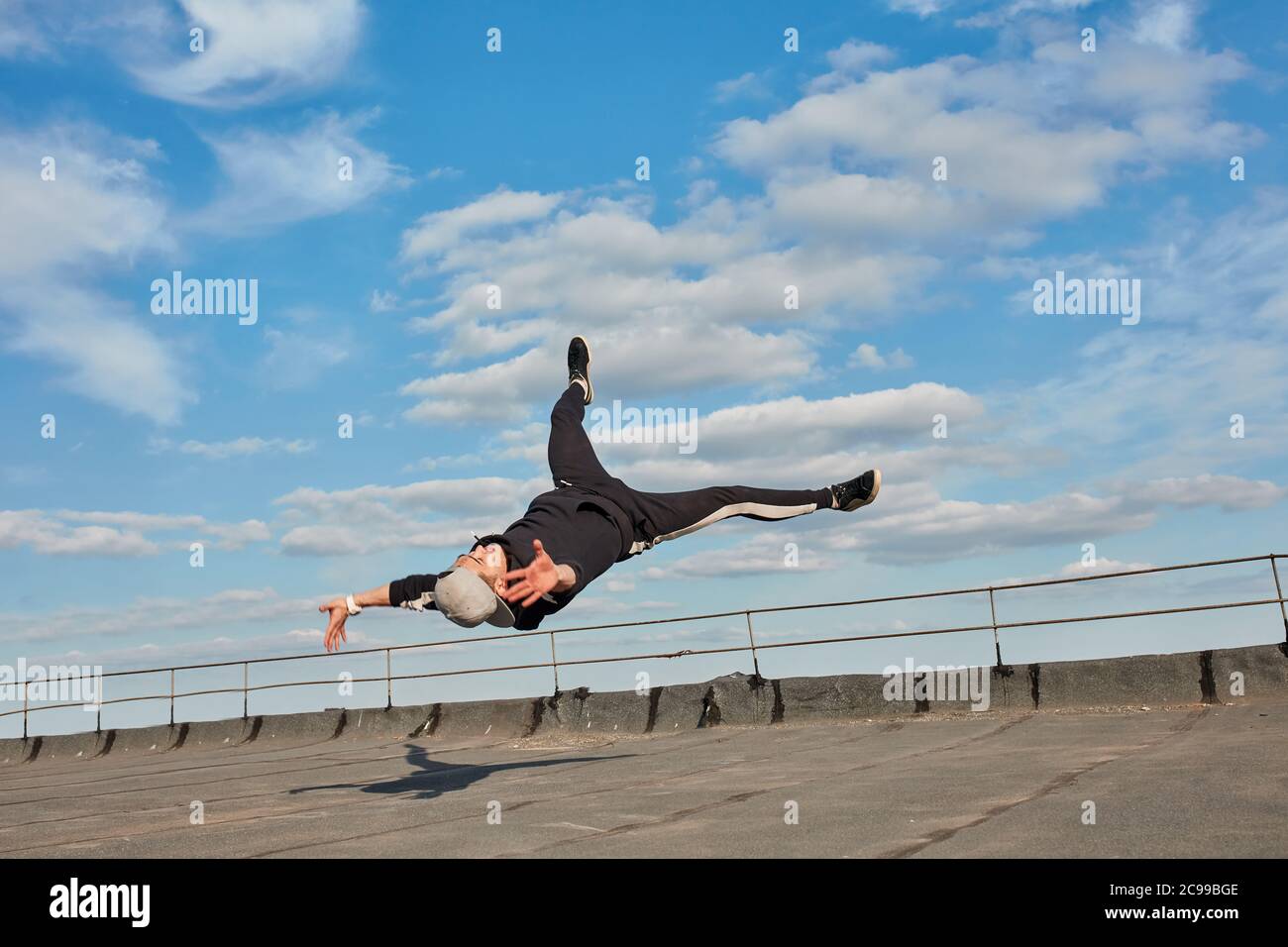 Street Dancer Hipster Kerl macht zurück Flip mit Arm Unterstützung. Asiatische Breakdancer Ausübung auf Dach. Low-Angle-Mid-Air-Ansicht vor blauem Himmel Hintergrund Stockfoto