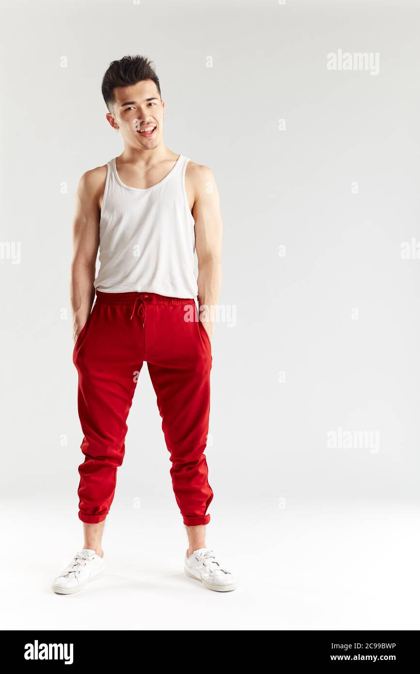 Junge sportliche stilvolle männliche Tänzerin in roten Jogginghosen posiert isoliert im Studio über weißem Hintergrund. Asiatische Hipster bboy lächelnd bei Kamera vor traini Stockfoto