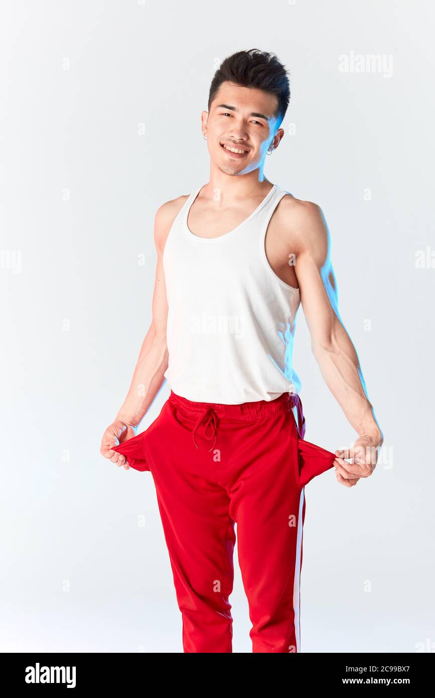 Junge sportliche stilvolle männliche Tänzerin in roten Jogginghosen posiert isoliert im Studio über weißem Hintergrund. Asiatische Hipster bboy lächelnd bei Kamera vor traini Stockfoto