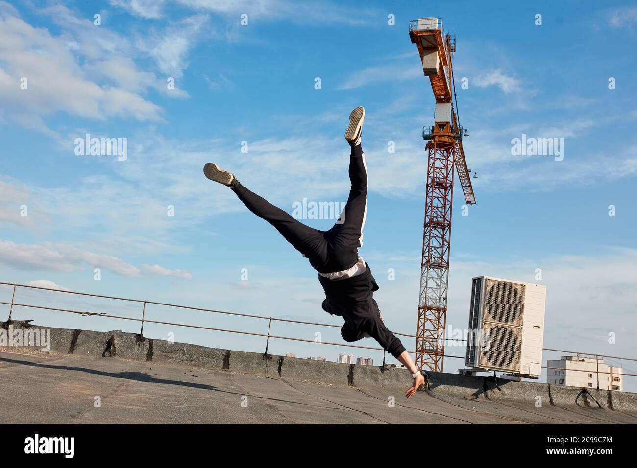 Free Style Tänzerin in schwarzen Kleidern fliegen in der Luft tun Coup Tanz Break Dance auf dem Dach des Gebäudes mit dem Baukran auf Hintergrund- Stockfoto