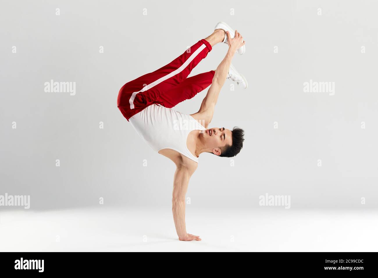 Junge koreanische männliche Tänzerin, die grundlegende Einfrierungen von Downrock Break ausführt, zeigt die Tanzbewegungen des zeitgenössischen Tanzes in sportlichen roten Trainingshosen für den Sport Stockfoto