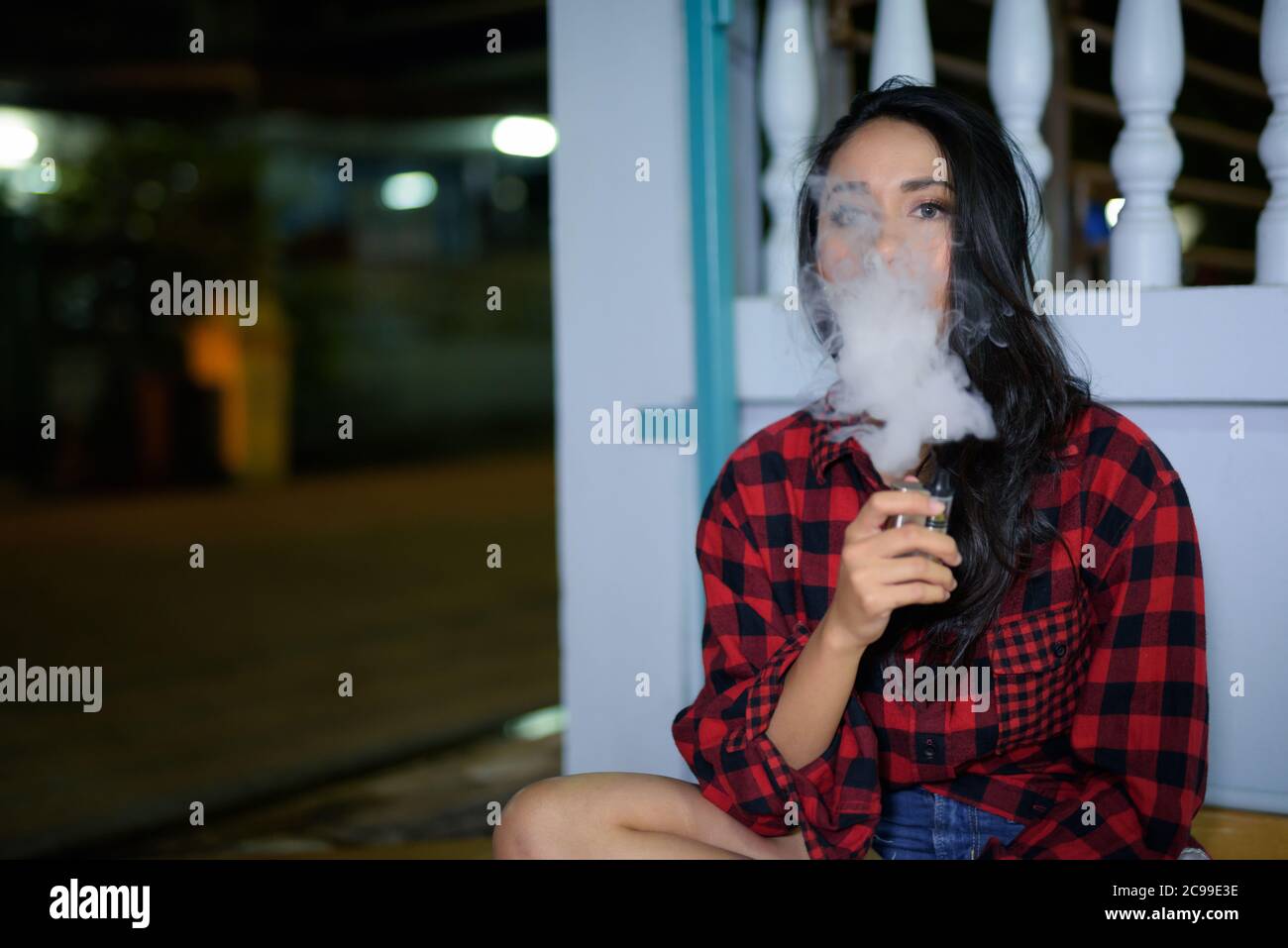 Junge schöne asiatische Frau dampfend zu Hause im Freien Stockfoto