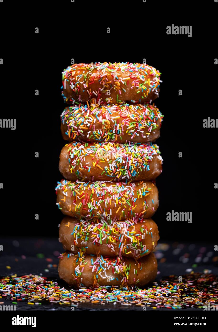 Donuts Berg mit Erdbeersirup und farbigen Belag auf schwarzem Hintergrund Stockfoto