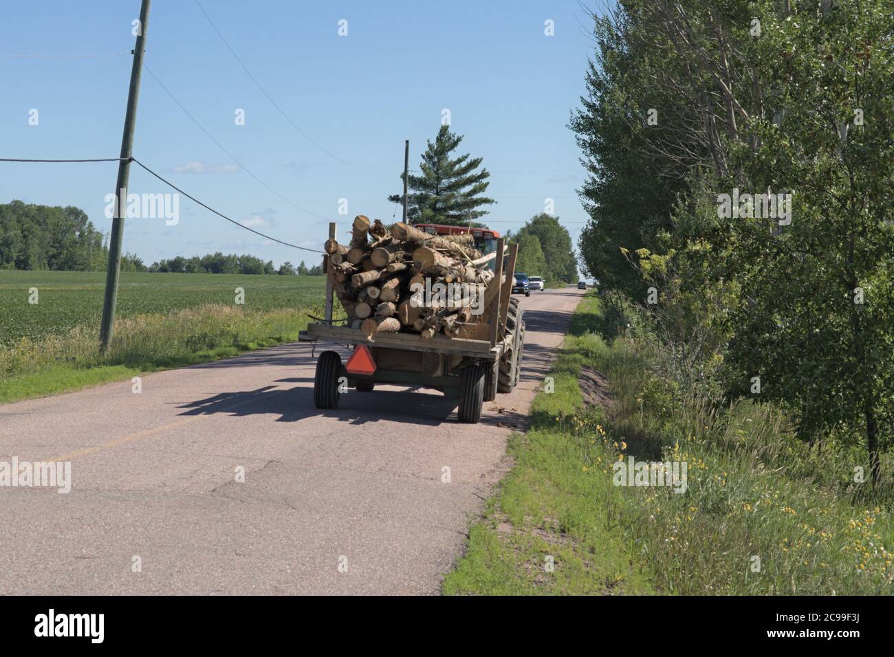 Traktor zieht einen alten Anhänger voller Brennholz die Straße hinunter Stockfoto