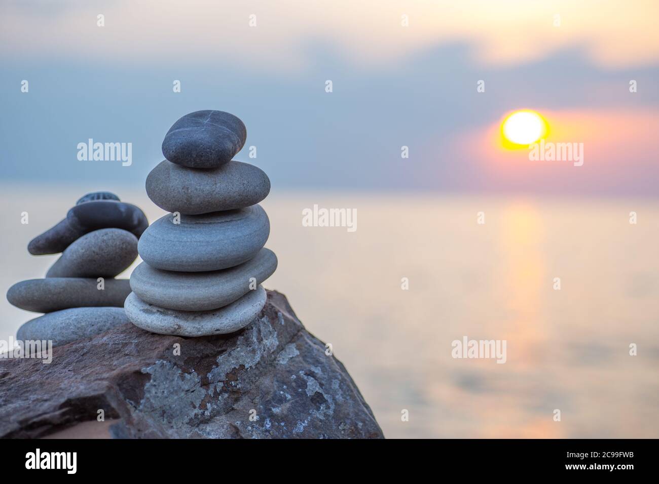 Steinpyramide auf Sand symbolisiert Zen, Harmonie, Gleichgewicht. Ozean bei Sonnenuntergang im Hintergrund. Stockfoto