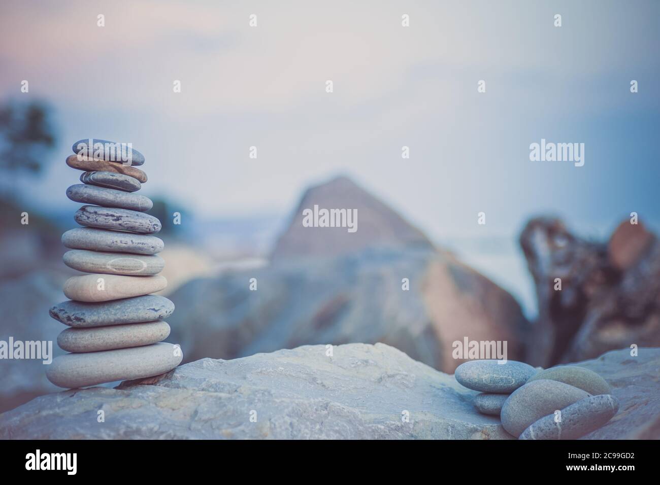Steinpyramide auf Sand symbolisiert Zen, Harmonie, Gleichgewicht. Ozean bei Sonnenuntergang im Hintergrund. Stockfoto