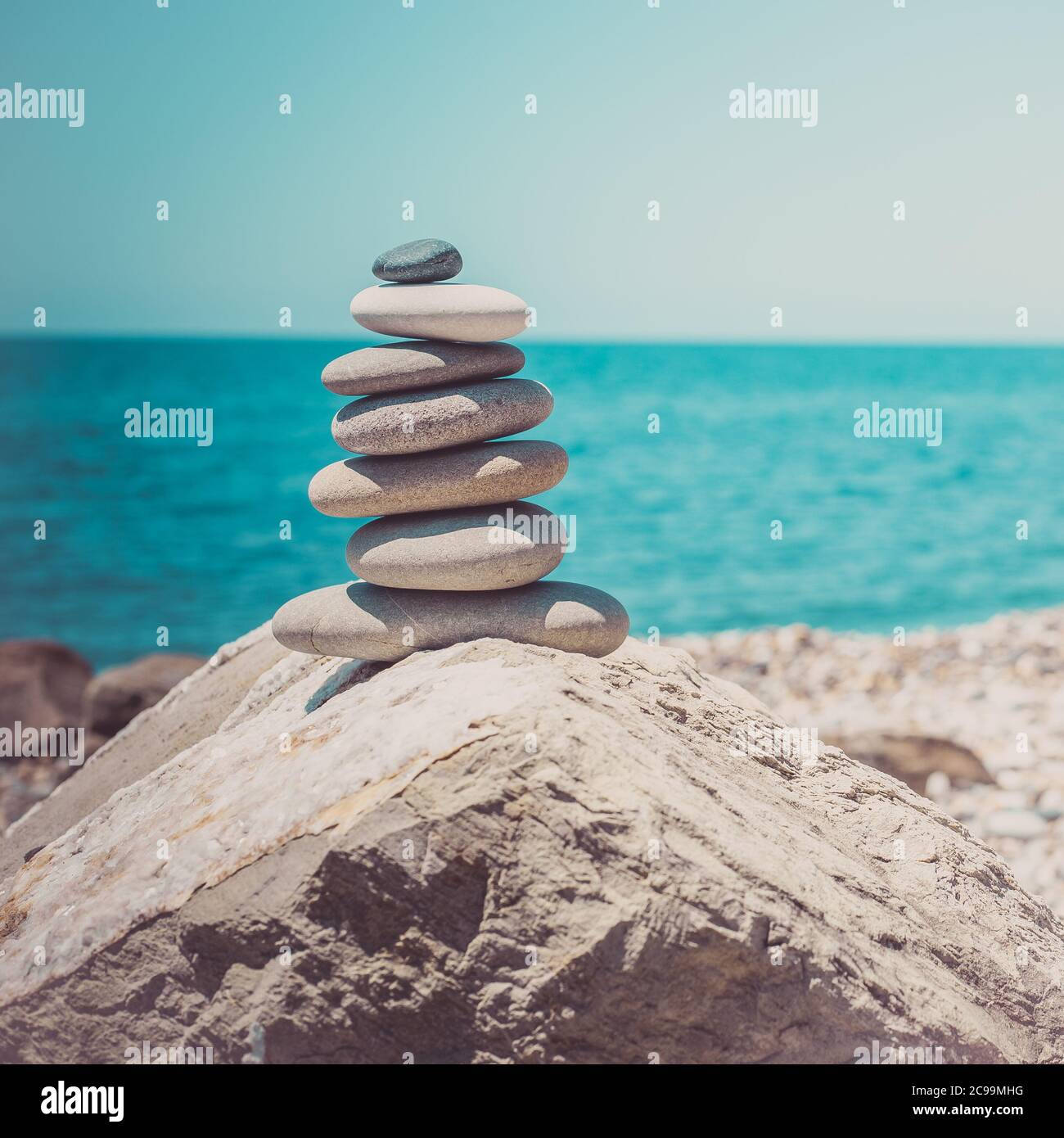 Steinen Pyramide auf Sand als Symbol für Zen, Harmonie und Balance. Meer bei Sonnenuntergang im Hintergrund Stockfoto