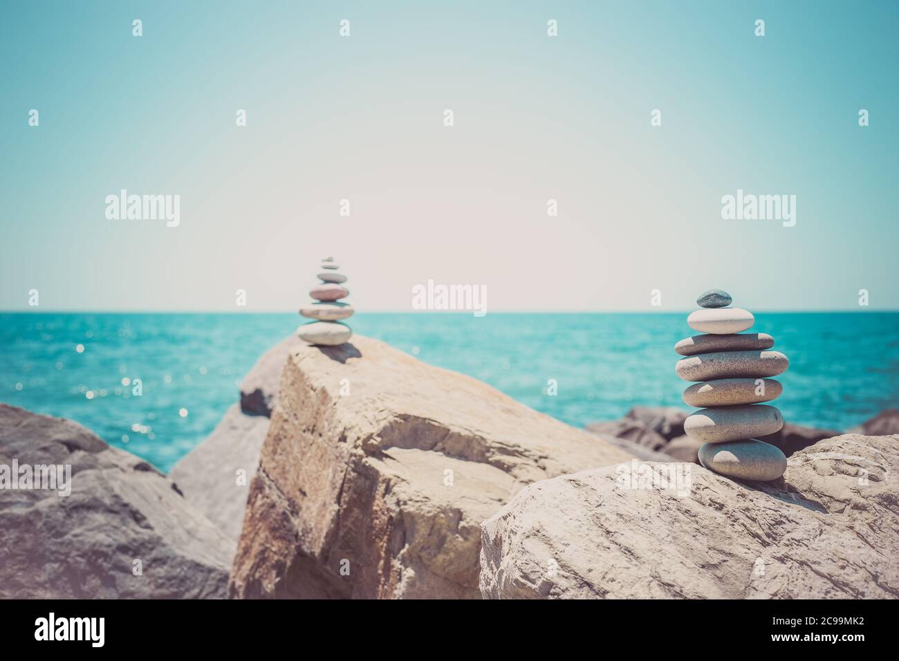 Steinen Pyramide auf Sand als Symbol für Zen, Harmonie und Balance. Meer bei Sonnenuntergang im Hintergrund Stockfoto