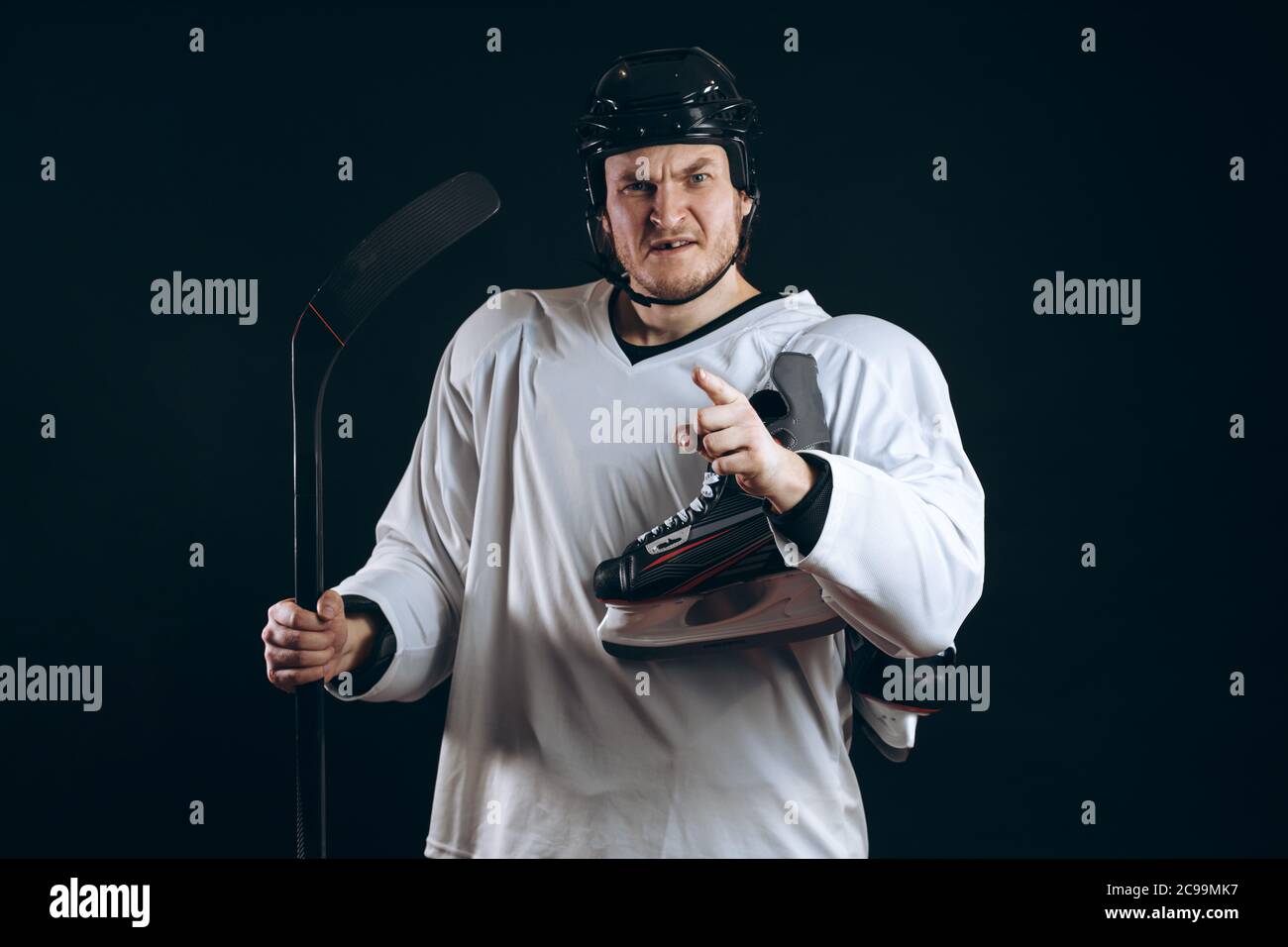 Porträt eines Professional Hockey Player in einer schützenden Sportswear und Helm mit Hockey Stick posiert und ein Skate in den Händen auf einem schwarzen Hintergrund. Stockfoto