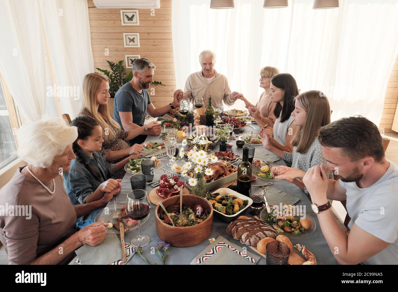 Große Familie am Tisch sitzend, Hände haltend und die Augen schließend, beten sie vor dem Essen Stockfoto