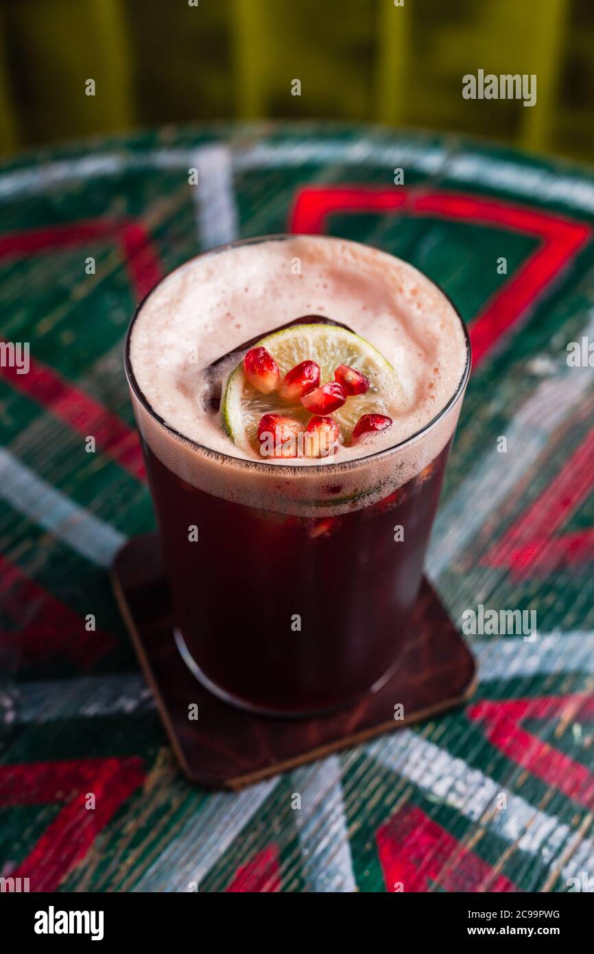 Ein Cocktail in einem Longdrinkglas mit Schaum, Eiswürfel innen, garniert mit einem Limettenrad und Granatapfelkernen Stockfoto