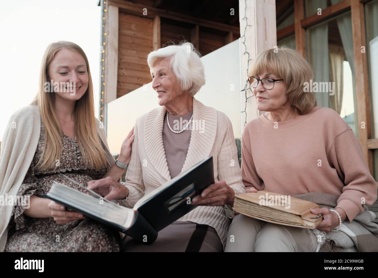 Zwei Großmütter zeigen ihrer Enkelin ihr Familienalbum, während sie draußen sitzen Stockfoto