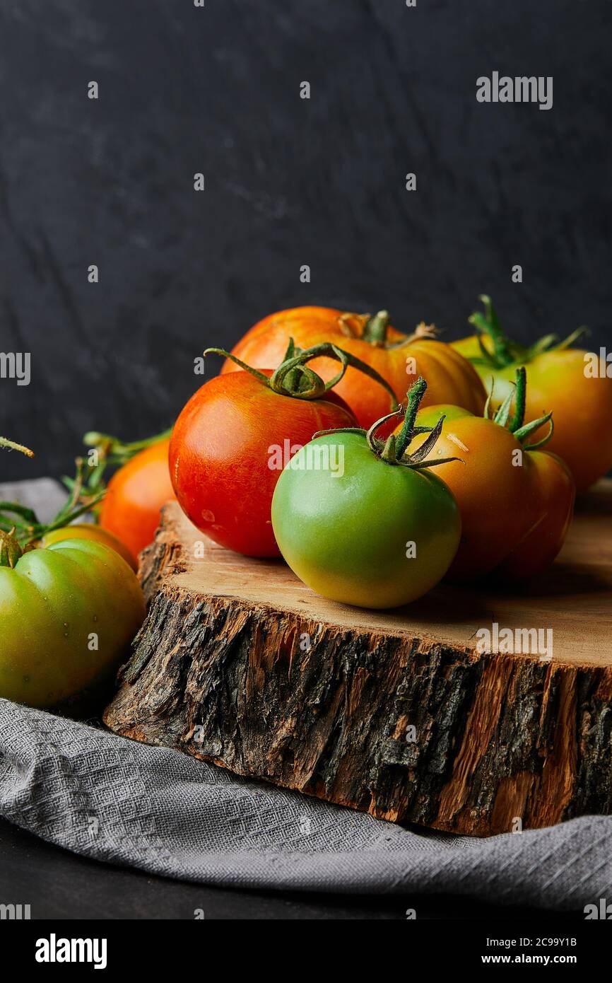 Vertikale Nahaufnahme von frischen grünen und roten Tomaten auf Ein Baumstumpf auf schwarzem Hintergrund Stockfoto