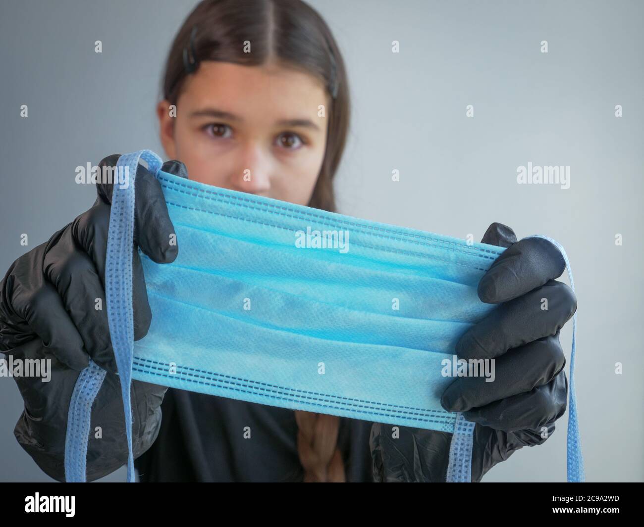 Weibliche Teenager-Mädchen in schwarzen Latexhandschuhen suchen in der Kamera, halten und zeigt eine blaue schützende medizinische Gesichtsmaske auf dem Vordergrund. Antiviral Stockfoto