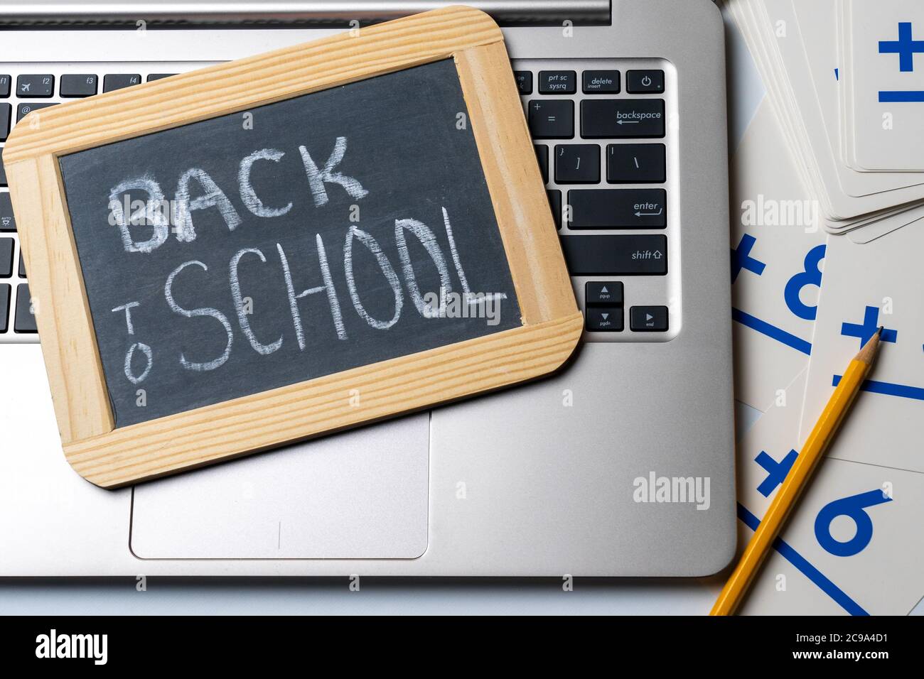 Zurück in die Schule geschrieben in Kreide auf einer kleinen Tafel auf einem Laptop-Computer mit einem gelben Bleistift und Karteikarten für das Konzept der alten Schule ve Stockfoto