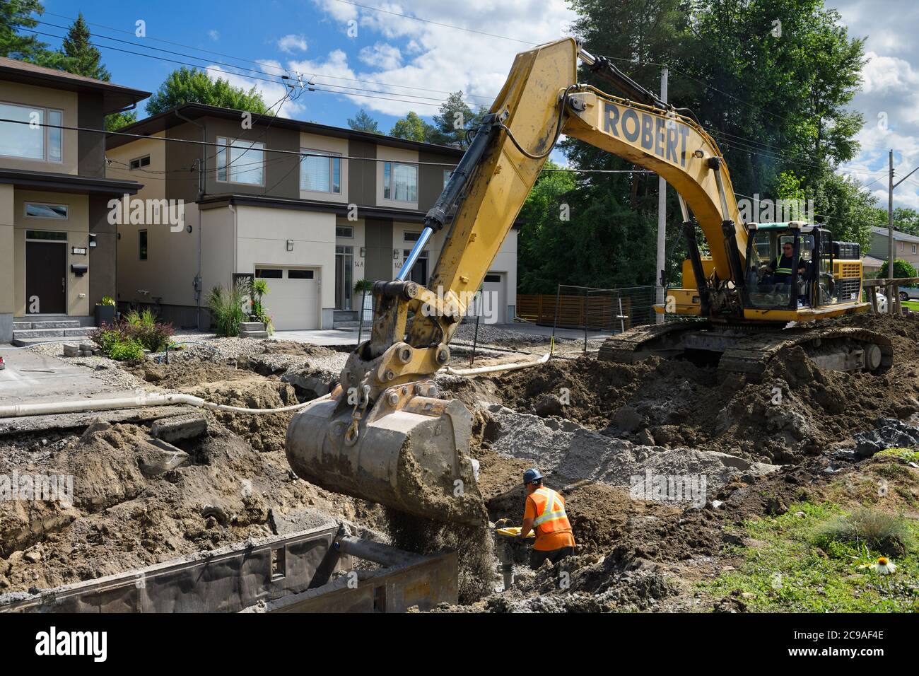 Arbeiter Stampfen Erde und Aggregat in Graben für neue Kanalinstallation mit Hilfe von Bagger auf Wohnstraße Nepean Ontario Stockfoto