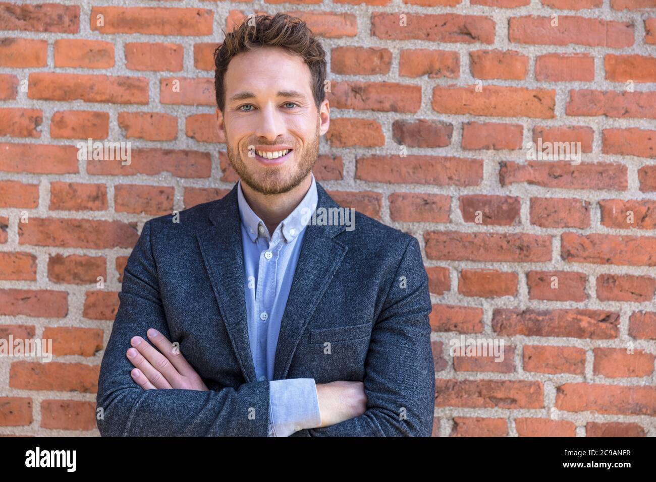Geschäftsmann Porträt zuversichtlich jungen Unternehmer Mann Blick auf Kamera gegen städtische Backsteinmauer Textur. Lächelnder kaukasischer männlicher Erwachsener Stockfoto