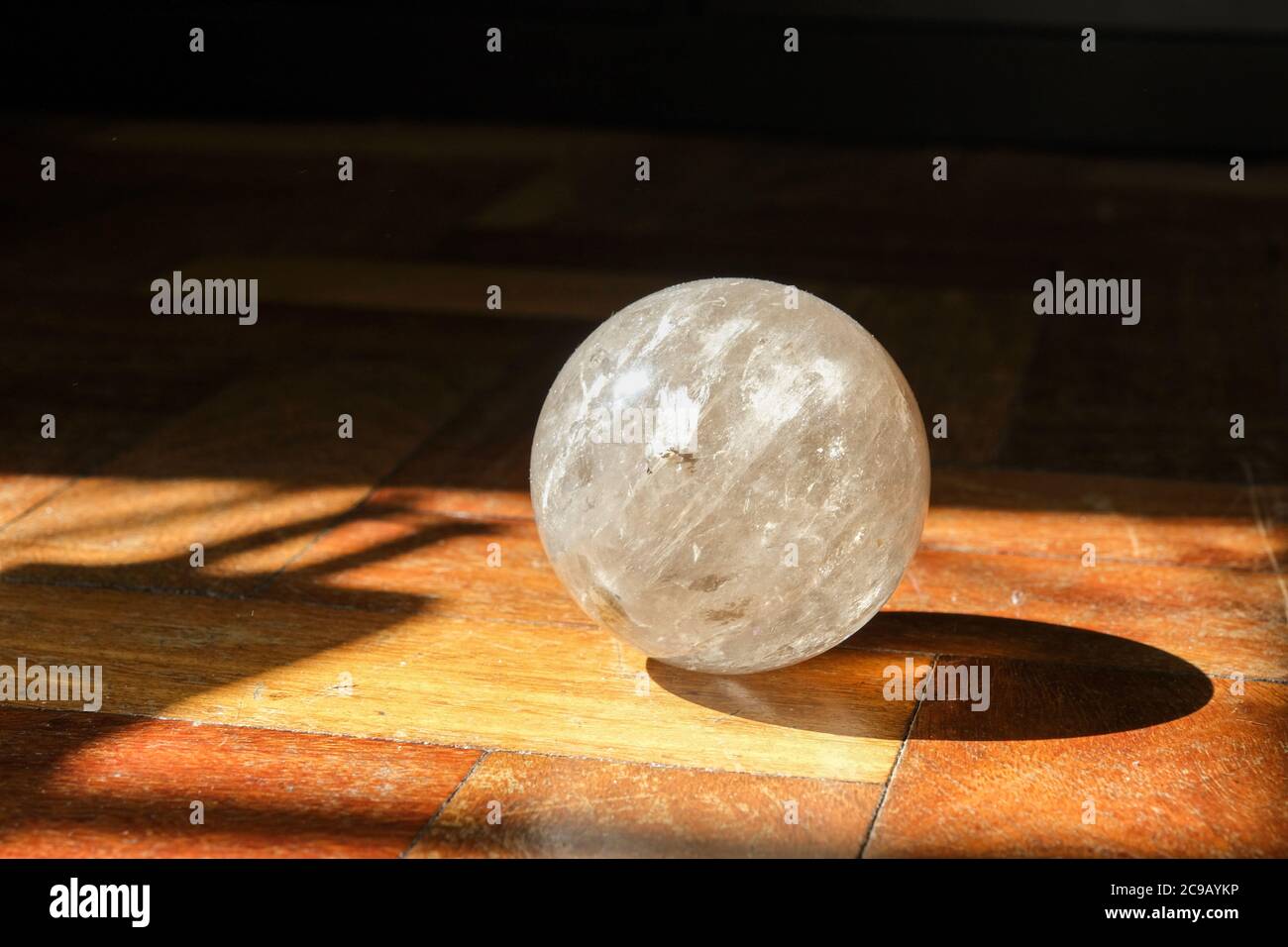 Rauchige Quarzkristall-Kugel, die in einer Sonnenflecke auf einem abgenutzten Holzparkettboden steht. Stockfoto