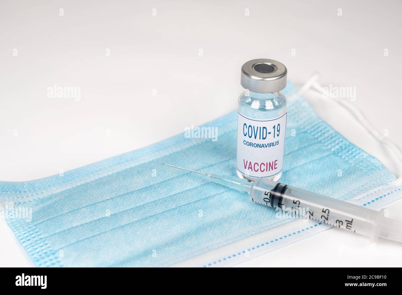 Medizinisches Konzept mit einer Spritze und einer Covid-19 Impfampulle über einer Einwegmaske. Stockfoto