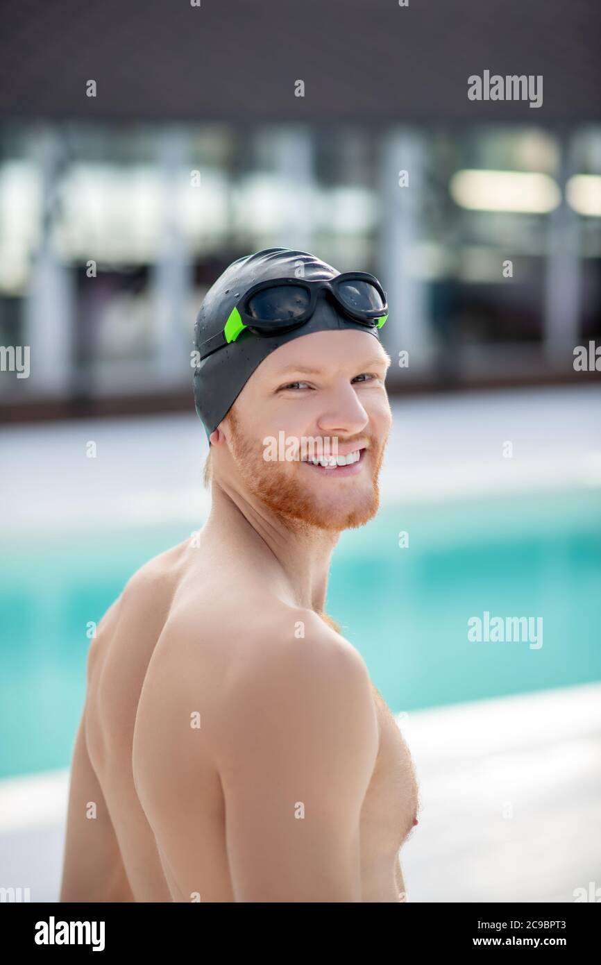 Fröhlicher junger Mann in Schwimmmütze, der auf halbem Weg schaut Stockfoto