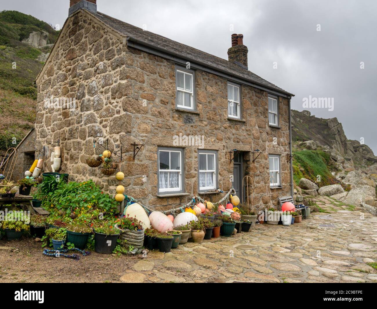 Altes Cornish Granitsteinhaus, dekoriert mit Fischerbooten und Topfpflanzen, Penberth Cove, Cornwall, Großbritannien Stockfoto