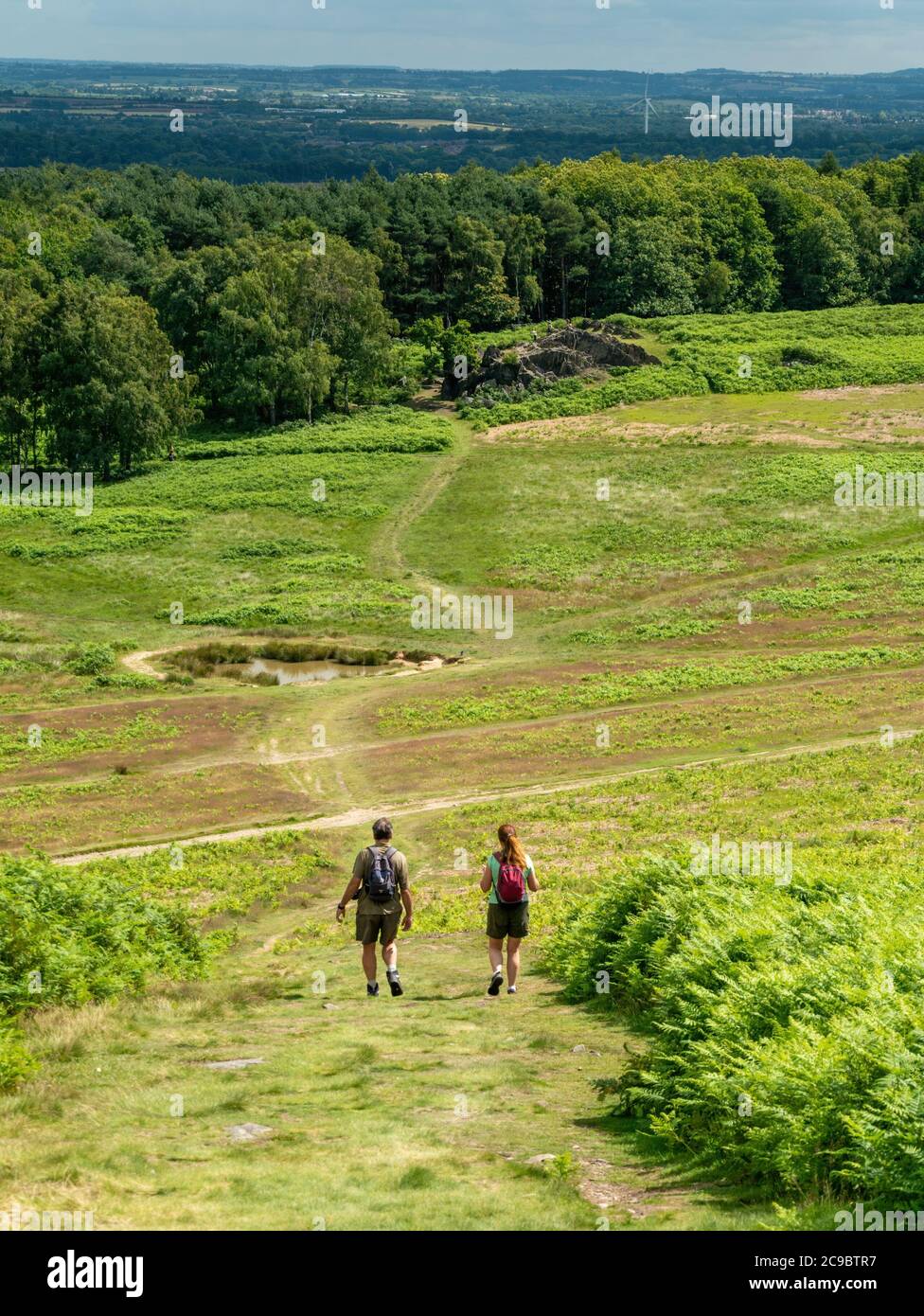 Ein paar Erwachsene Wanderer in Sommerkleidung mit Rucksäcken zu Fuß bergab in Bradgate Park an einem warmen Sommertag, Leicestershire, England, Großbritannien Stockfoto