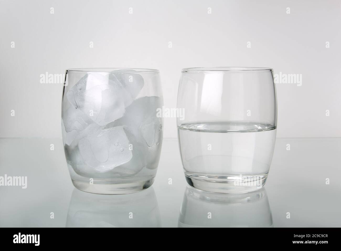 Foto von zwei Gläsern. Ein Glas voll Eis und ein zweites Glas halb voll Wasser, um das geschmolzene Eis zu zeigen. Fotografiert auf einem hellen Hintergrund. Stockfoto