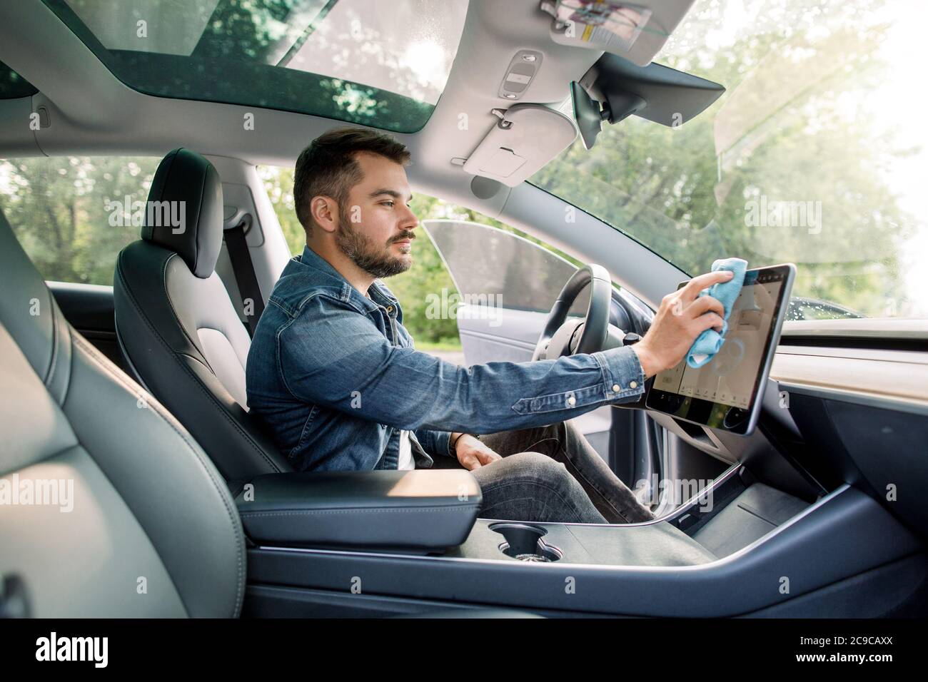 Reinigungszeit, Auto Detaillierung Konzept. Porträt von jungen schönen kaukasischen Mann mit Bart sitzt in seinem modernen selbststeuernden Auto und wischen Staub Stockfoto