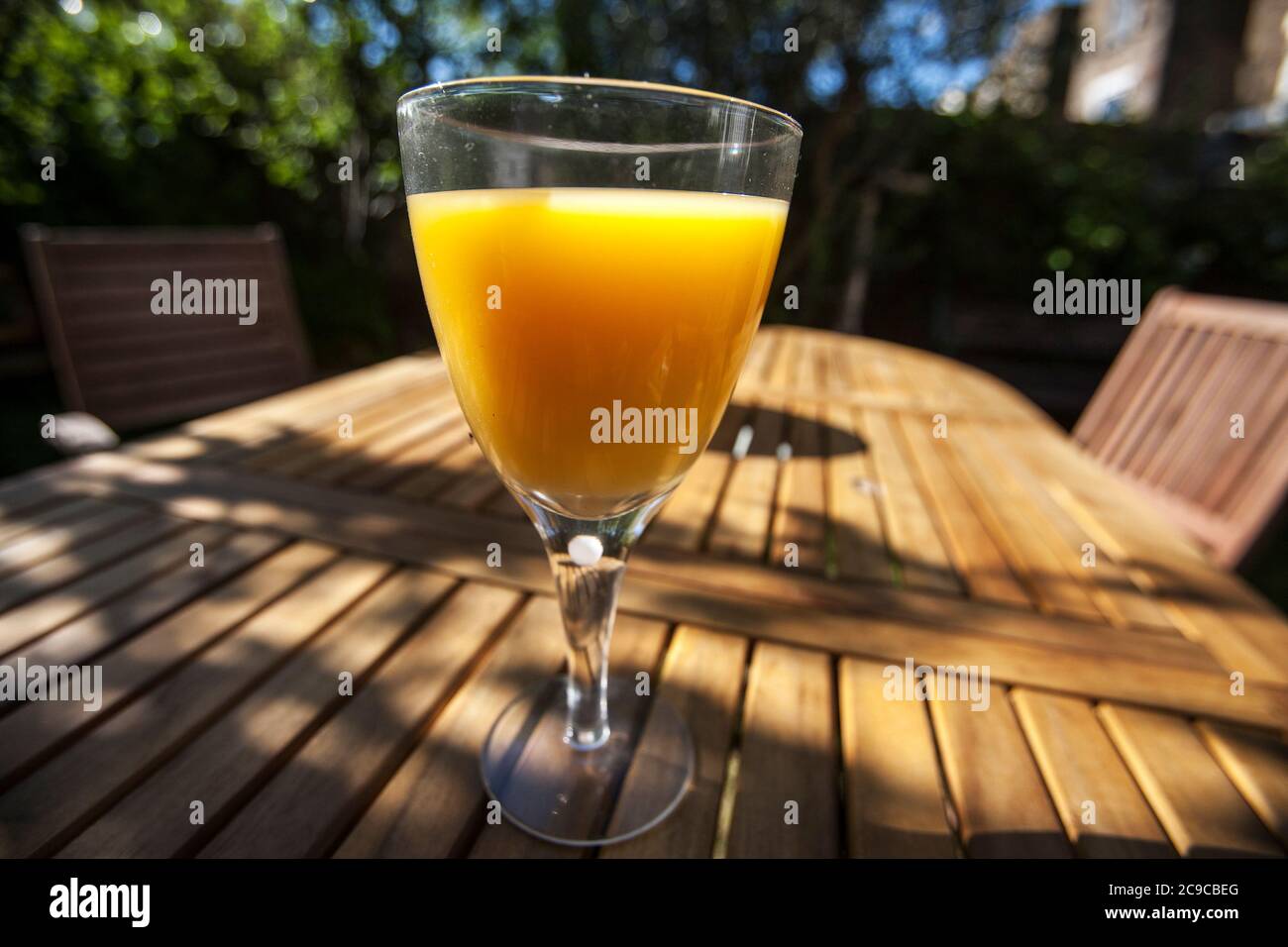 Glas Orangensaft, Holzgartentisch, neben weißem Globenlicht, Stockfoto