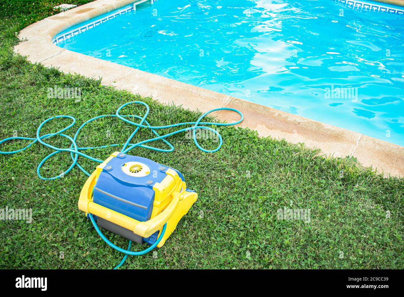 Automatischer Poolreiniger mit Elektroschlauch auf Gras und frisch gereinigtem Pool geschützt Stockfoto
