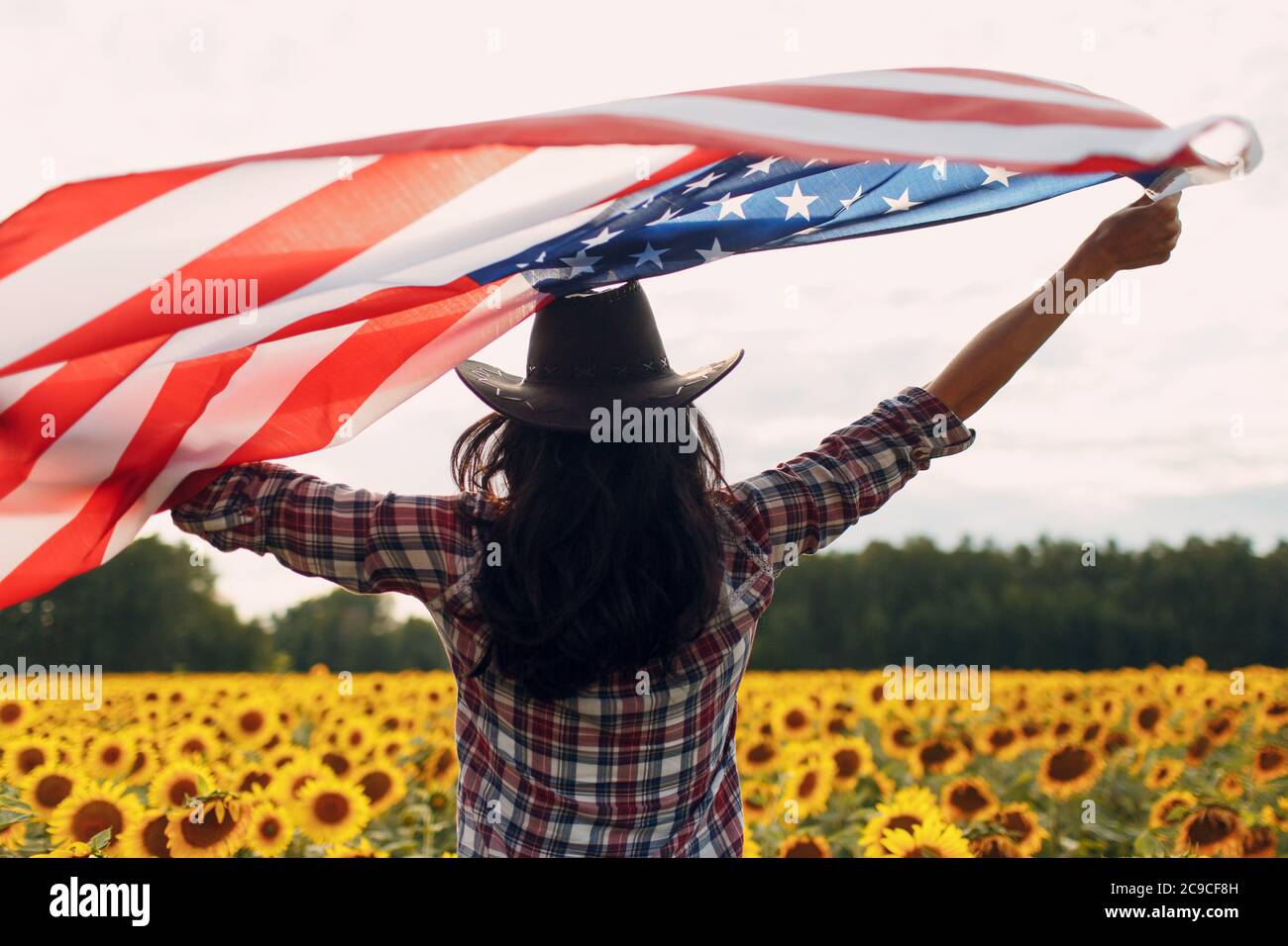 Junge Frau mit Flagge der Vereinigten Staaten von Amerika im Sonnenblumenfeld. 4. Juli Independence Day USA Konzept. Stockfoto