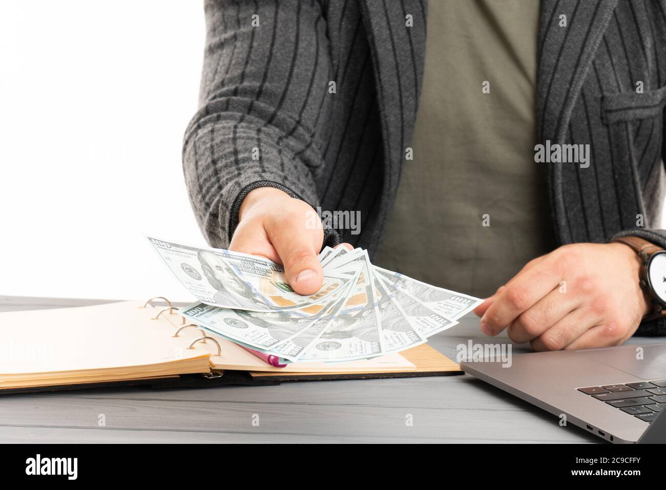 Mann in Anzug hält in einem Arm Pack von hundert Dollar Rechnungen, während Sie am Tisch sitzen Stockfoto