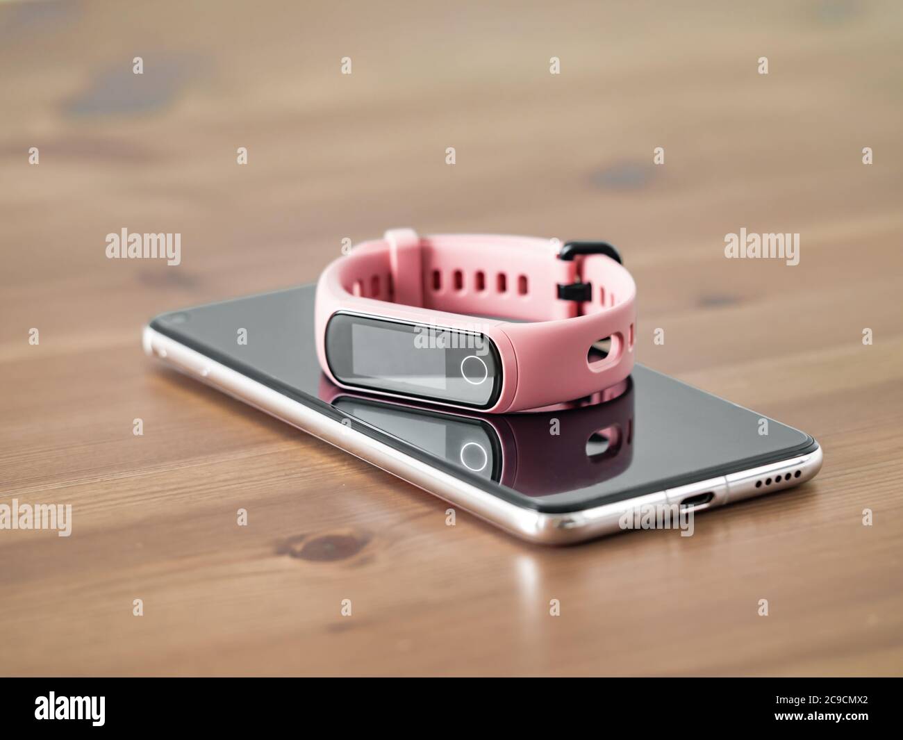 Fitness-Tracker auf Smartphone-Holztisch. Rosa weibliche Schrittzähler oder tragbares Gerät auf Smartphone mit Infinity-Display, Kopierraum Stockfoto