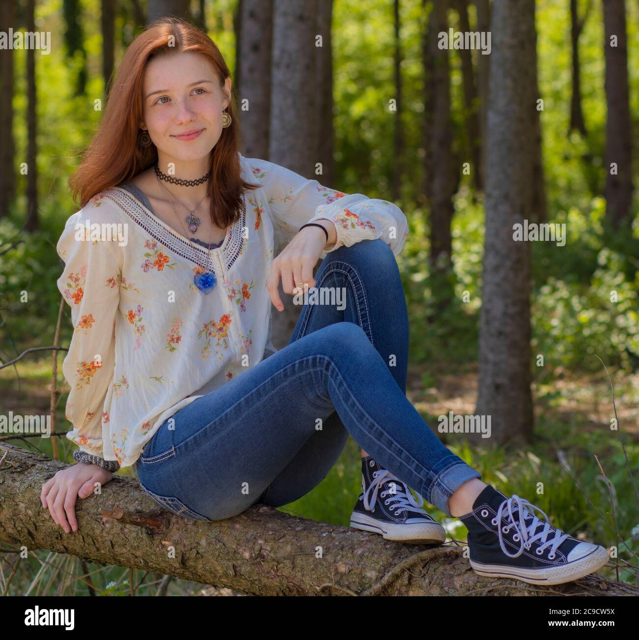 Hübsche Teenager oder junge Erwachsene Weibchen mit dunkelrotem Haar, hellem Fell und blaugrünen Augen, die in legerer Kleidung auf Log in Summer Pennsylvania Woods posieren Stockfoto